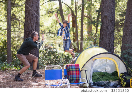 Father photographing playful boy jumping at campsite 32331860