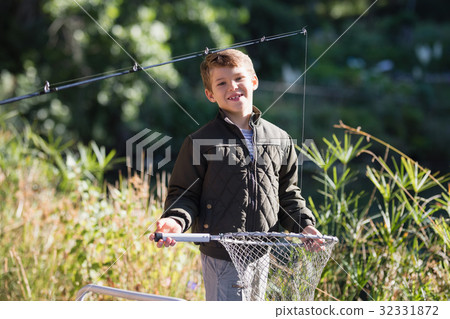 Portrait of smiling boy holding fishing net while standing in forest 32331872