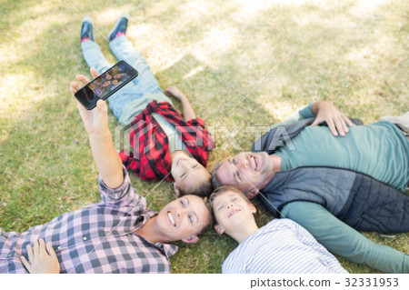 Happy family lying on the grass and taking selfie 32331953