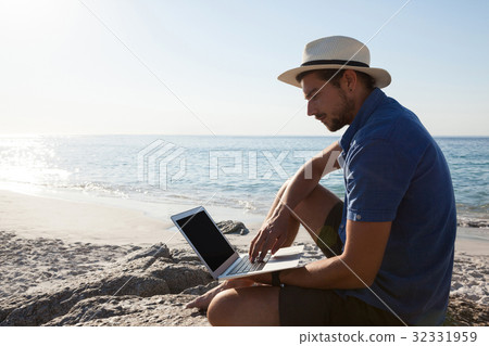 Man sitting on the rocks and using laptop on beach Man sitting on the rocks and using laptop on beach 32331959