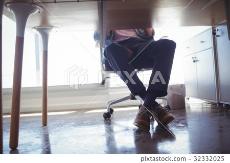 Low section of businessman sitting at desk in office Low section of businessman sitting at desk in office 32332025