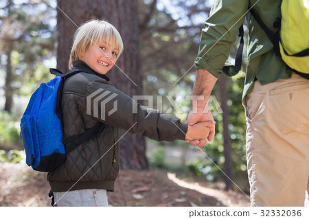 Happy boy holding fathers hand while hiking in forest Happy boy holding fathers hand while hiking in forest 32332036