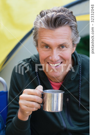 Man holding cup by tent at campsite Man holding cup by tent at campsite 32332048