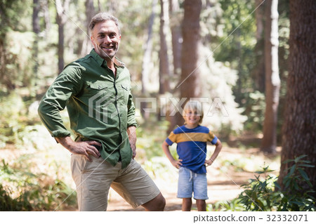 Father and son with hands on hips standing in forest Father and son with hands on hips standing in forest 32332071