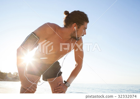 Exhausted man taking a break after jogging on beach 32332074