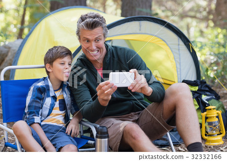 Father and son taking picture by tent in forest Father and son taking picture by tent in forest 32332166