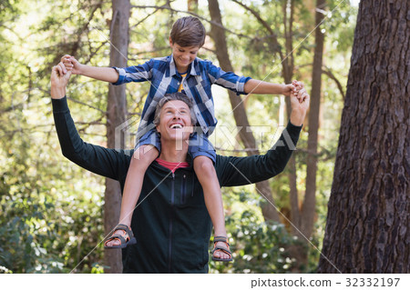 Cheerful father carrying son on shoulders in forest Cheerful father carrying son on shoulders in forest 32332197