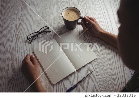Businesswoman holding coffee cup on desk in office 32332319
