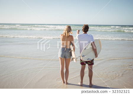Rear view of couple holding surfboards while standing at beach 32332321