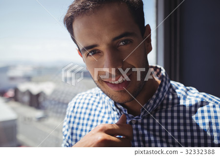 Portrait of young businessman by window in office Portrait of young businessman by window in office 32332388