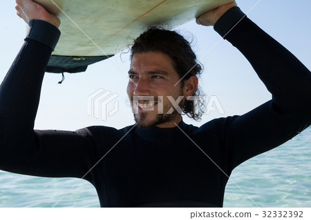 Surfer in wetsuit carrying surfboard over head at beach coast Surfer in wetsuit carrying surfboard over head at beach coast 32332392