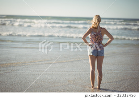 Rear view of woman standing with hands on hip at beach Rear view of woman standing with hands on hip at beach 32332456