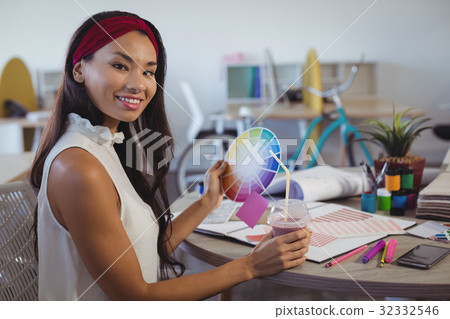 Portrait of businesswoman holding colour swatch and drink at office Portrait of businesswoman holding colour swatch and drink at office 32332546