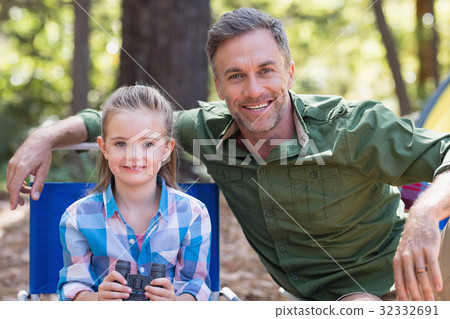 Happy father and daughter sitting at campsite in forest 32332691