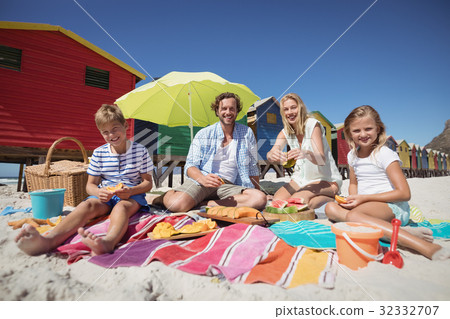 Portrait of happy family sitting together on blanket at beach Portrait of happy family sitting together on blanket at beach 32332707