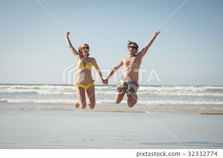 Cheerful couple holding hands while jumping at beach 32332774