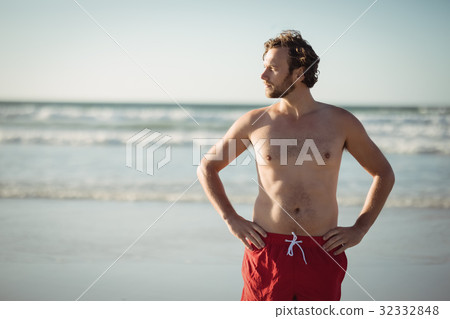 Thoughtful shirtless man standing with hands on hip at beach Thoughtful shirtless man standing with hands on hip at beach 32332848