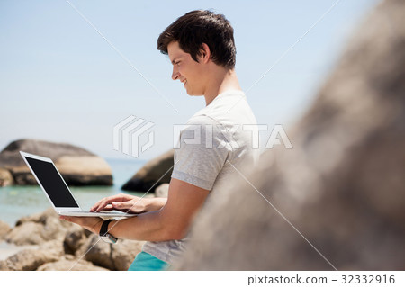 Man leaning on the rocks and using laptop at the sea coast 32332916