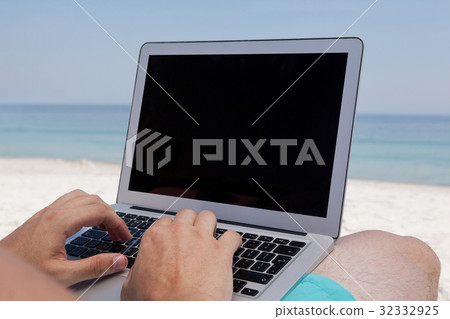 Man using laptop while resting at beach Man using laptop while resting at beach 32332925