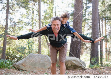 Cheerful father piggybacking son while hiking in forest Cheerful father piggybacking son while hiking in forest 32333013