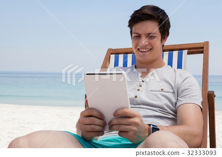 Man sitting on sunlounger and using digital tablet on the beach 32333093