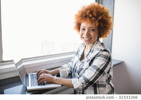 Portrait of smiling businesswoman using laptop on window sill 32333266