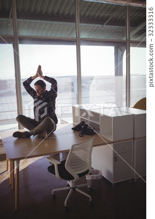 Businessman meditating on desk at office Businessman meditating on desk at office 32333316