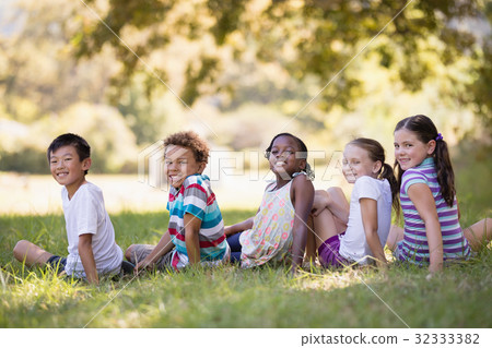 Smiling friends sitting on grass at campsit Smiling friends sitting on grass at campsit 32333382