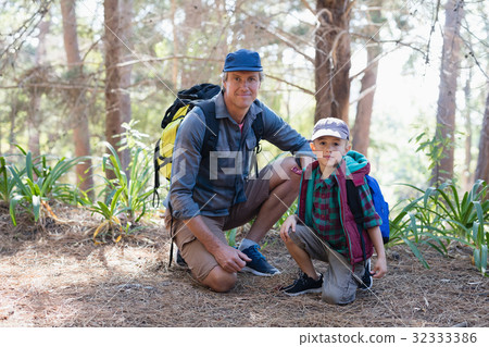 Portrait of father and son kneeling in forest 32333386