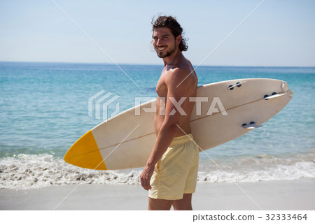 Smiling surfer with surfboard standing at beach coast Smiling surfer with surfboard standing at beach coast 32333464