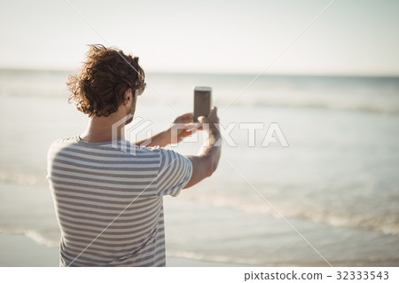 Rear view of man photographing sea at beach 32333543