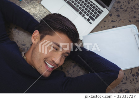 Smiling businessman lying by laptop and clipboard at office 32333727