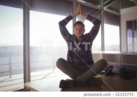 Young businessman meditating on table at office 32333755