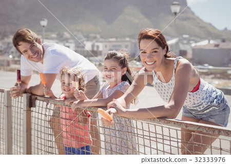 Portrait of happy family holding ice cream by railing Portrait of happy family holding ice cream by railing 32333976
