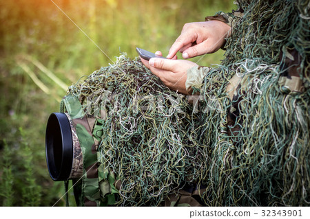 ornithologist in the ghillie suit using smartphone ornithologist in the ghillie suit using smartphone 32343901