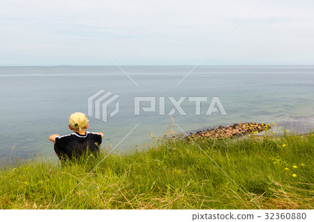 Boy sitting on te edge of a scarp, above the sea Boy sitting on te edge of a scarp, above the sea 32360880