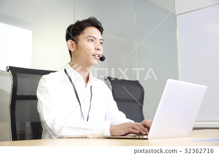 A young man who supports telephone while operating a personal computer A young man who supports telephone while operating a personal computer 32362716