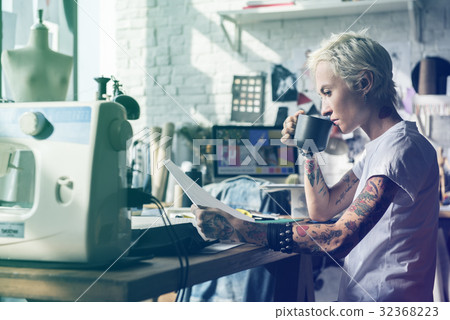 Fashion designer tattooed girl drinking and looking at sketch 32368223