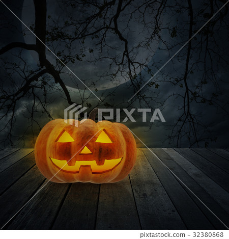 Jack O Lantern pumpkin on floor over dead tree 32380868