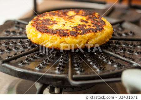 Arepa (Corn bread) being roasted on a round grill 32431671