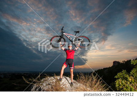 Cyclist raising the mountain bike above his head with success Cyclist raising the mountain bike above his head with success 32449412