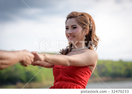 woman in red dress is holding hands with young man 32470233