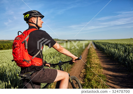 圖庫照片: young man riding on a bicycle on green meadow with