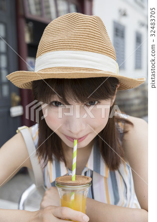 A woman drinking orange juice at an open cafe 32483705