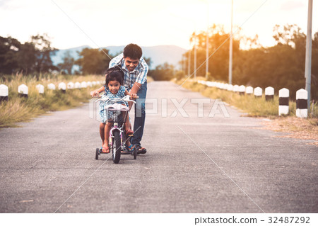 Asian girl having fun to ride bicycle with father 32487292