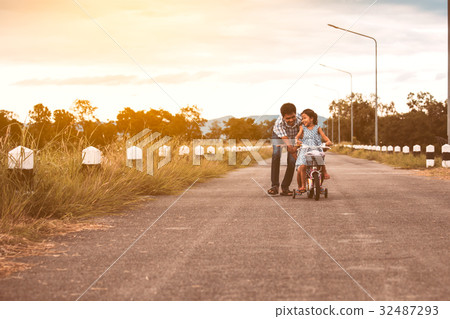 Asian girl having fun to ride bicycle with father 32487293