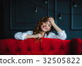pretty brunette young woman posing behind red sofa 32505822