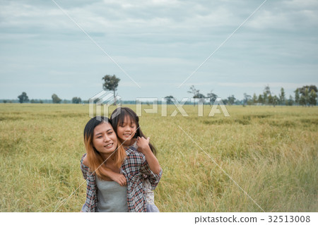 Mother giving daughter ride on back in park. 32513008