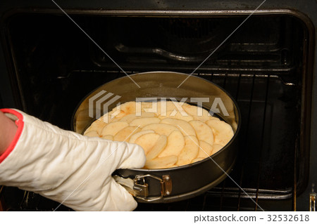 Close up of woman putting apple pie inside oven with gloves in her hand 32532618