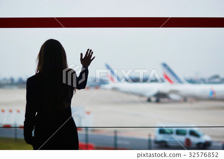 Woman with hand luggage in international airport, looking through the window at planes 32576852